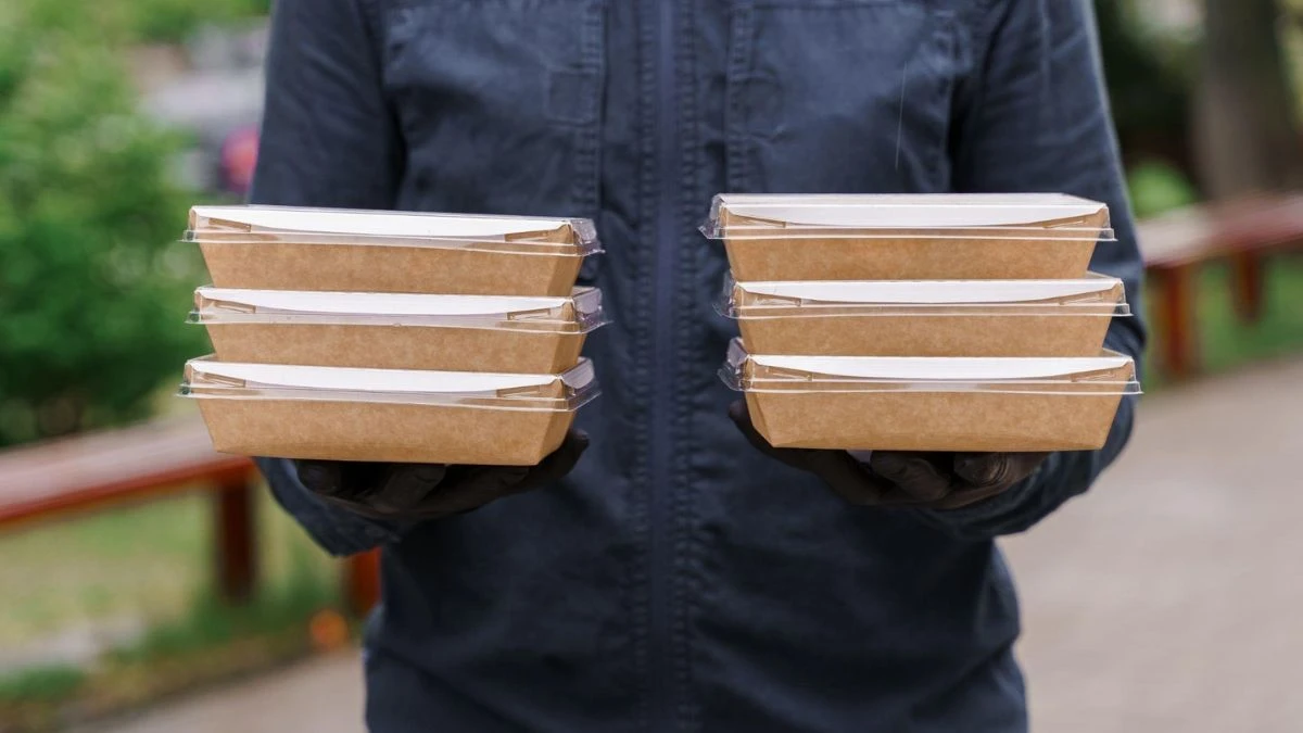 Homem segurando várias caixas de comida para entrega, ideal para serviços de delivery. As embalagens são de papel reciclável, mostrando preocupação ambiental.