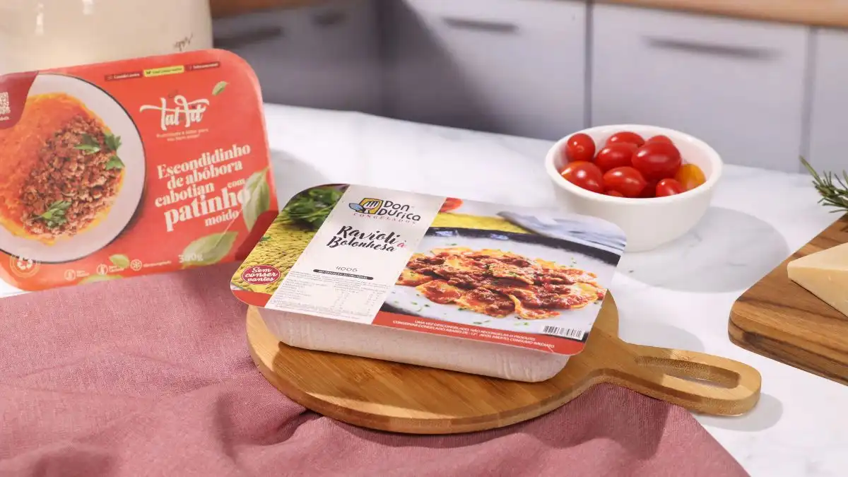 Imagem de pratos prontos para refeição, incluindo escondidinho de abóbora e ravioli, apresentados em embalagens atraentes sobre uma mesa.