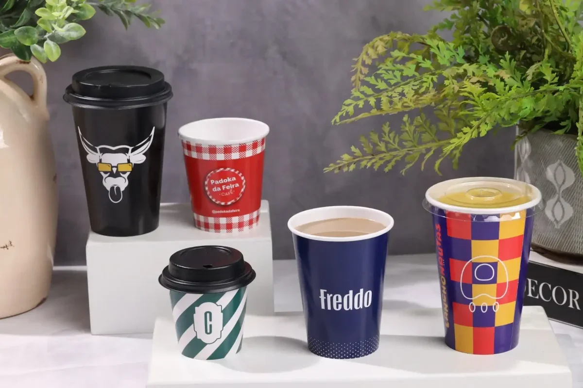 Variações de copo antivazamento de café decorados sobre uma superfície branca, mostrando designs variados e atraentes para bebidas quentes e frias.