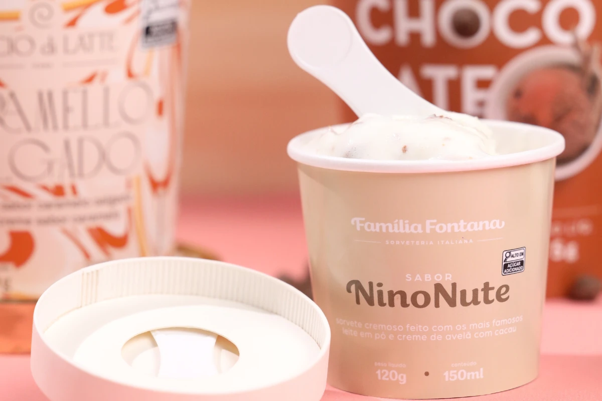 Saiba como a pazinha de sorvete pode ser um diferencial Sorvete-de-chocolate-branco-NinoNute-da-Familia-Fontana-com-embalagem-aberta-em-uma-mesa-com-uma-pazinha-de-sorvete.-O-fundo-com-outros-produtos-de-chocolate-e-leite