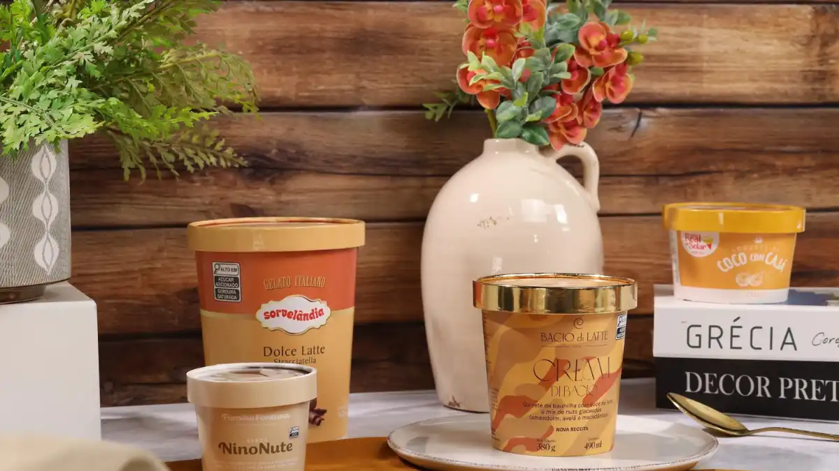 Variedade de sabores de sorvetes artesanais em potes de sorvetes decorados, com fundo de parede de madeira e vasos de plantas, ideal para sobremesas geladas