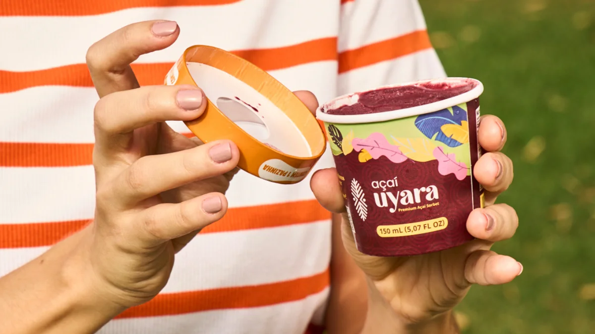 Mãos segurando pote aberto de sorvete de açaí Uýara em ambiente externo