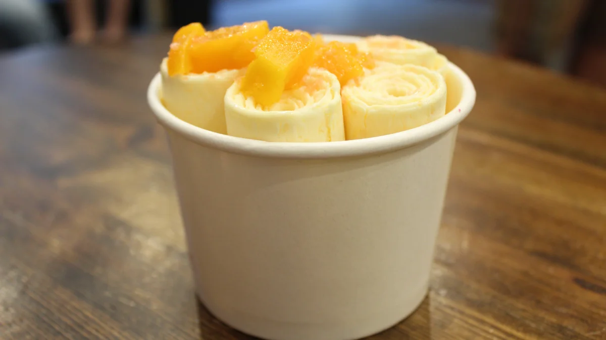 Rolinho de sorvete de creme com pedaços de manga em copo branco