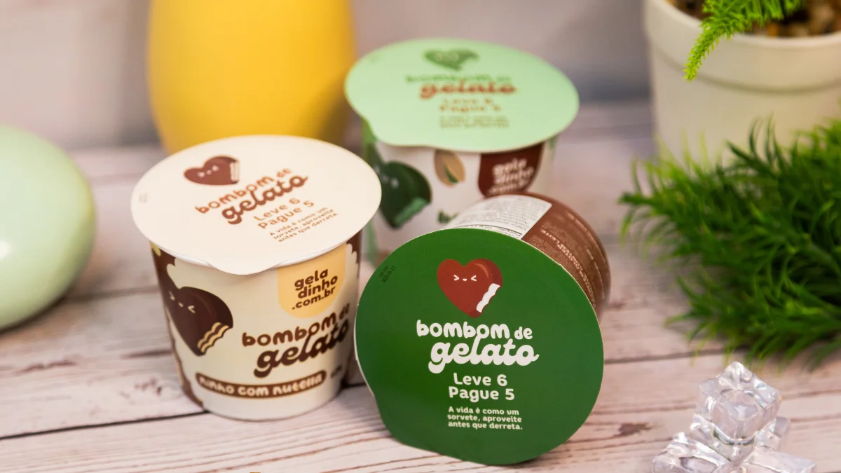 Pote de sobremesa personalizado da Apolo Embalagens em três opções de cor e sabor, que estão sobre uma mesa de madeira.